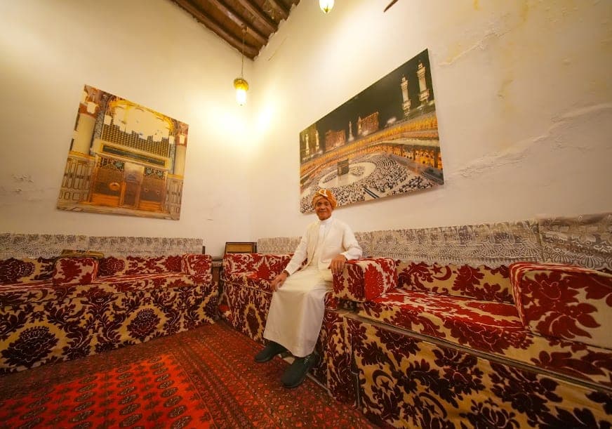 A wide majlis with red carpet and a painting hung on the wall